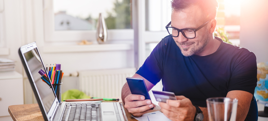 Man entering card details on his phone with laptop