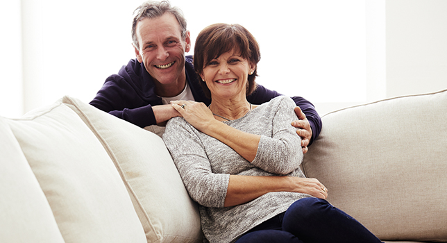 happy mature couple holding hands on couch 