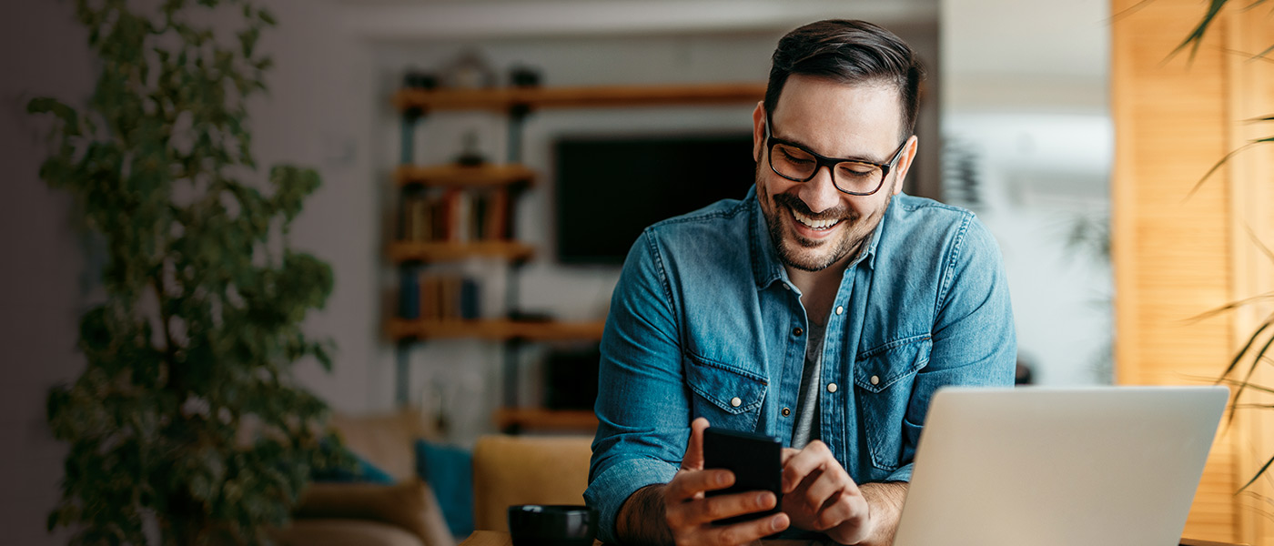 Smiley man on his laptop and phone topping up his Foresters ISA