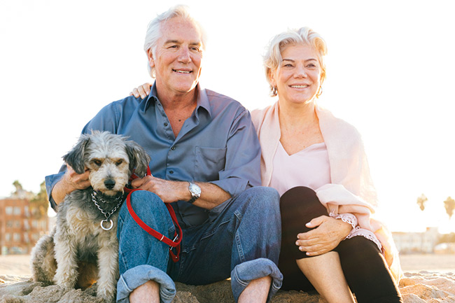 Happy retired couple with a Foresters Pension Plan at the beach with their dog