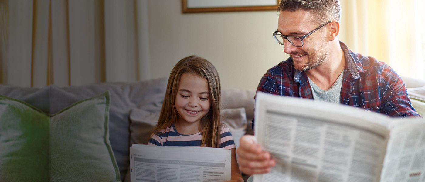 Dad and daughter sitting on sofa reading newspapers