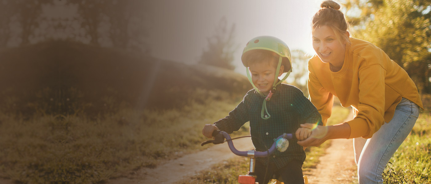 Happy mother with personal insurance cover teaching her son to ride a bike