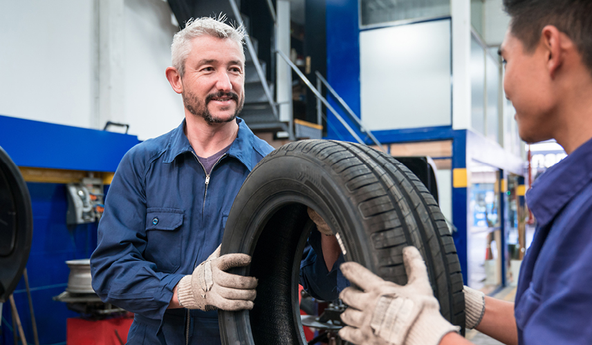 Two mechanics passing tire to each other